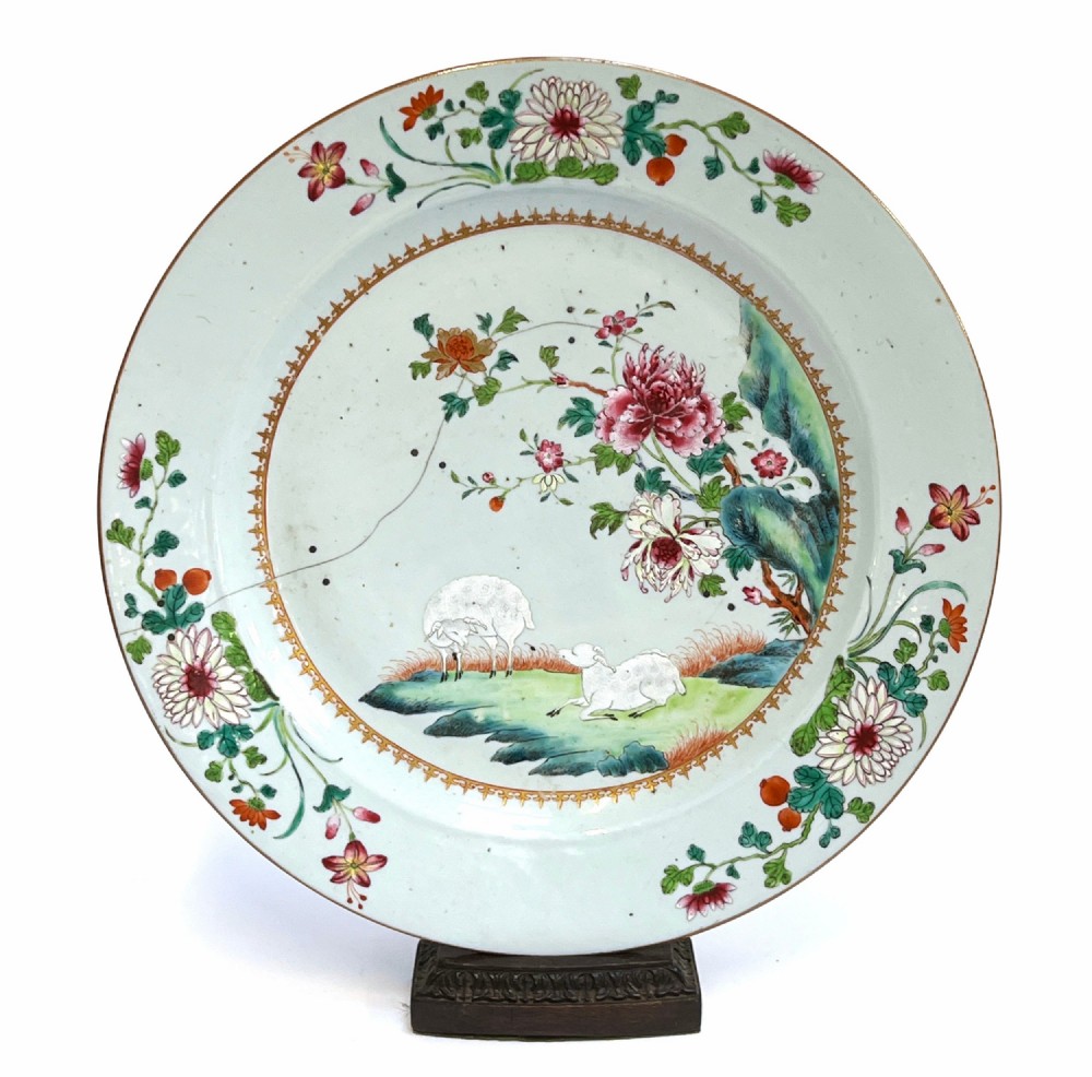 A large circular Chinese export porcelain charger plate hand-painted with famille rose floral motifs, rockwork, and two white sheep on a pale background.