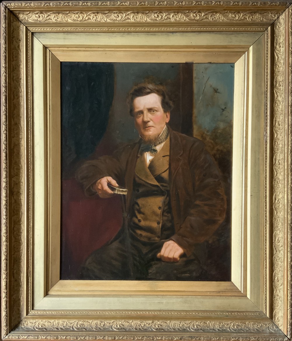 A 19th-century oil painting depicting a seated gentleman in a brown coat and waistcoat holding a small book, encased in an ornate gilded frame.