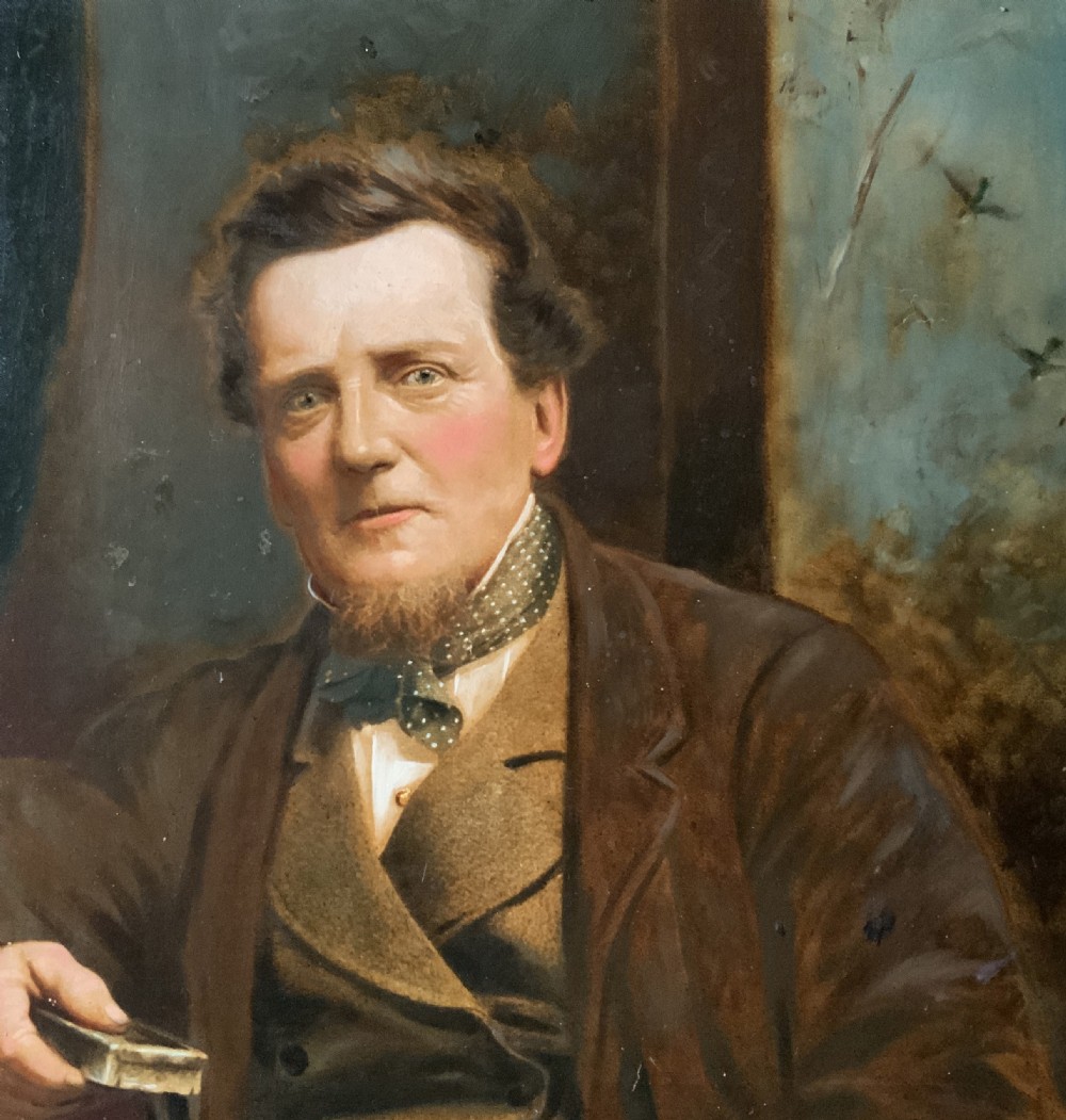 A 19th-century oil painting depicting a seated gentleman in a brown coat and waistcoat holding a small book, encased in an ornate gilded frame. View V