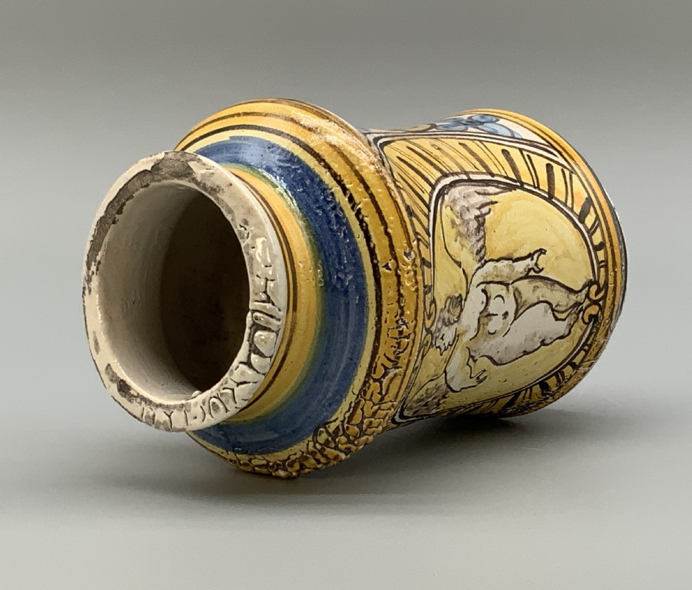 A waisted cylindrical tin-glazed majolica albarello jar decorated in yellow, blue, and dark brown hand-painted pigments featuring a central winged figure motif. View XI
