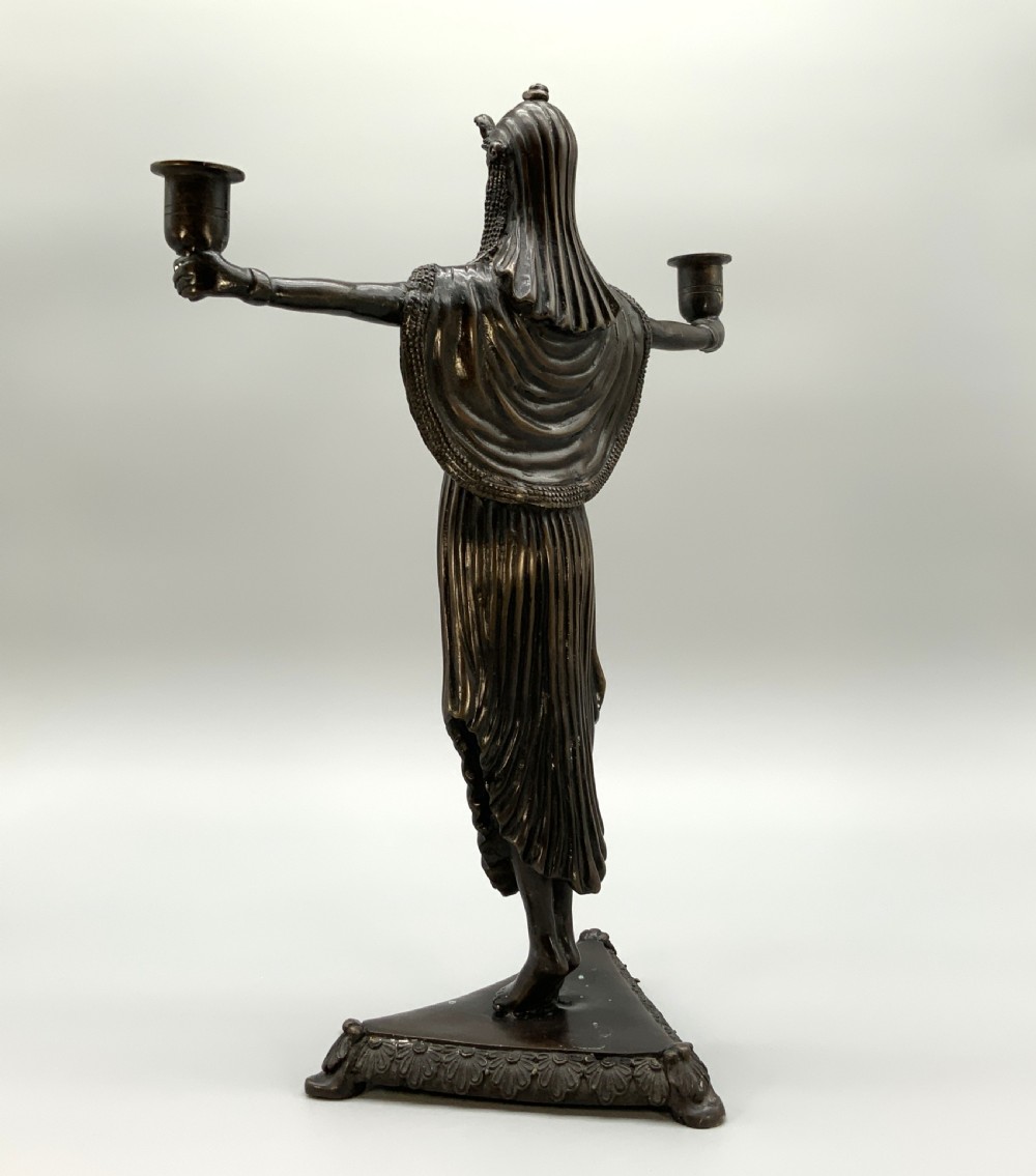 A patinated bronze Egyptian Revival candelabra featuring a female figure with outstretched arms holding two candle sockets, standing on a decorated triangular base. View VIII