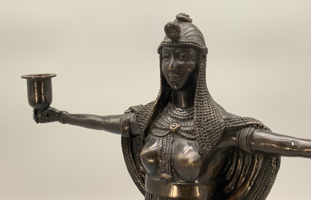 A patinated bronze Egyptian Revival candelabra featuring a female figure with outstretched arms holding two candle sockets, standing on a decorated triangular base. View IX