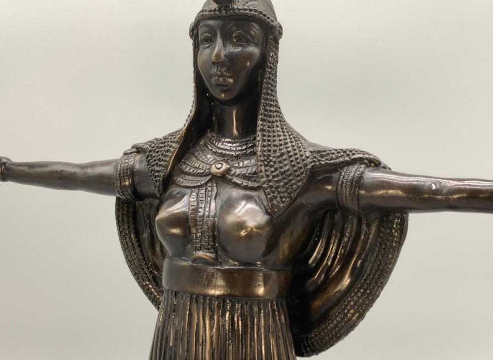 A patinated bronze Egyptian Revival candelabra featuring a female figure with outstretched arms holding two candle sockets, standing on a decorated triangular base. View X