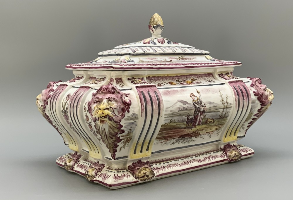 An antique French faience covered soup tureen featuring hand-painted pastoral scenes in manganese purple, moulded lion mask side handles, and a stepped lid with a finial. View IV