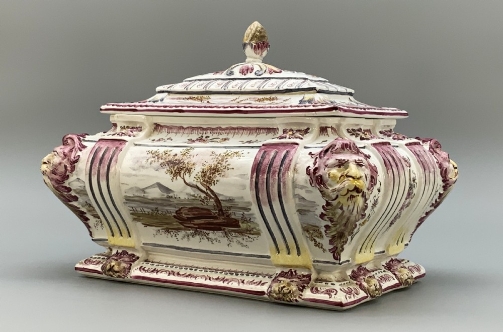 An antique French faience covered soup tureen featuring hand-painted pastoral scenes in manganese purple, moulded lion mask side handles, and a stepped lid with a finial. View VI