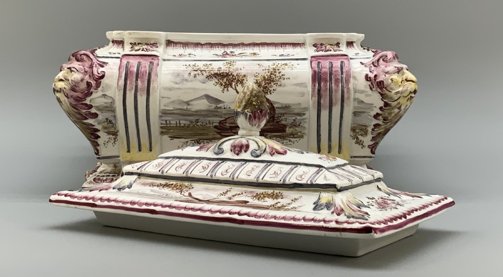 An antique French faience covered soup tureen featuring hand-painted pastoral scenes in manganese purple, moulded lion mask side handles, and a stepped lid with a finial. View X