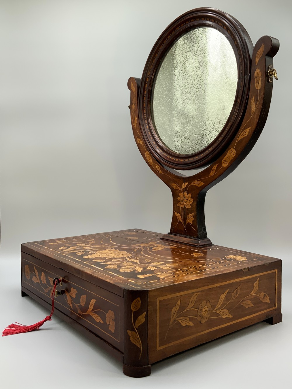 A 19th-century Dutch marquetry toilet mirror featuring a circular swivelling glass frame supported by carved wooden arms above a single base drawer decorated with detailed floral timber inlays. View VIII
