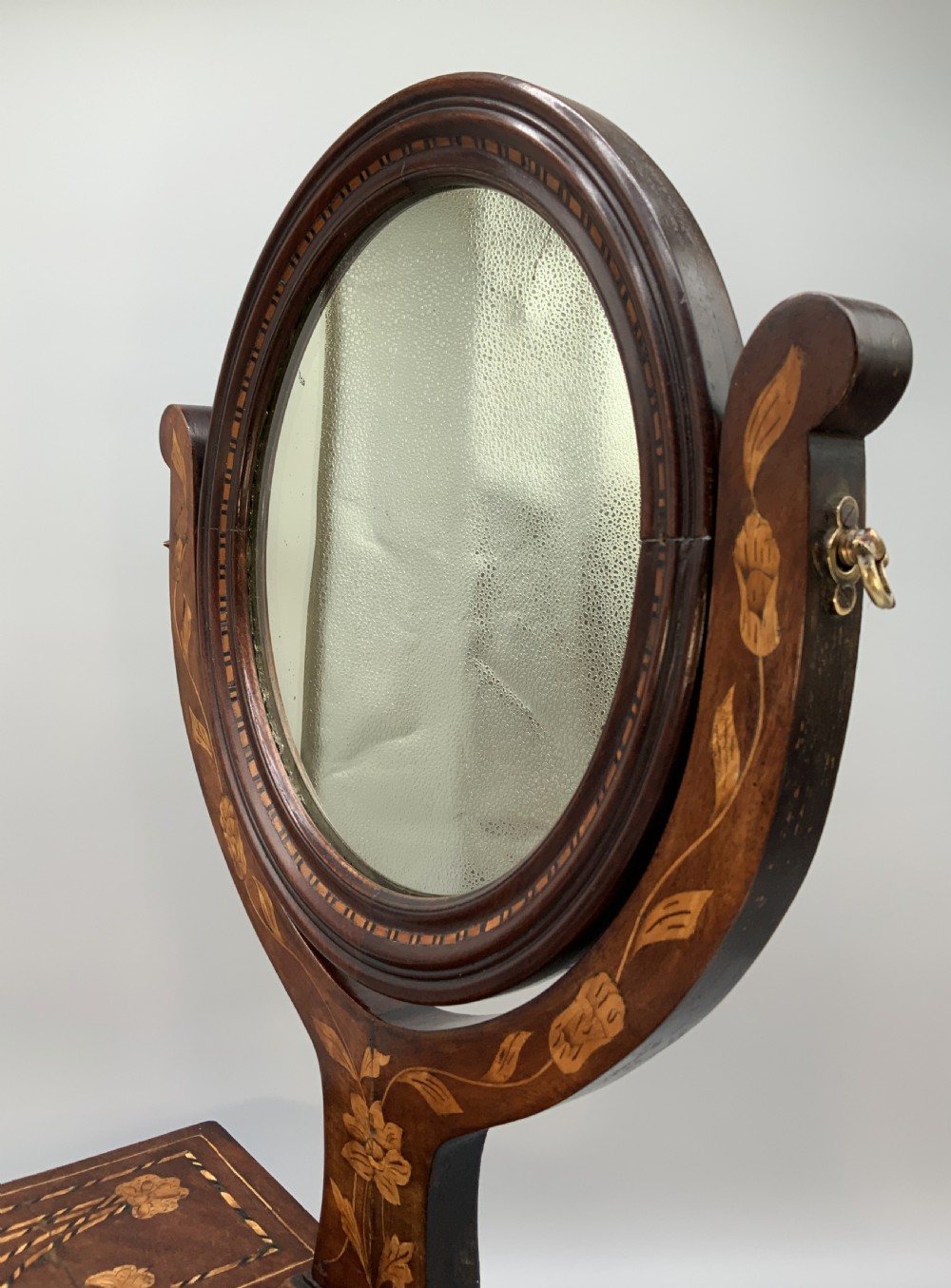 A 19th-century Dutch marquetry toilet mirror featuring a circular swivelling glass frame supported by carved wooden arms above a single base drawer decorated with detailed floral timber inlays. View IX