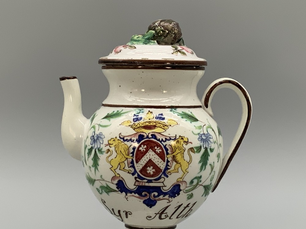 An 18th-century Italian tin-glazed earthenware pharmacy wet drug jug with a spouted body, top handle, lid with sculpted finial, painted armorial crest, floral scrolls, and Latin text reading Syr Alth. View IV