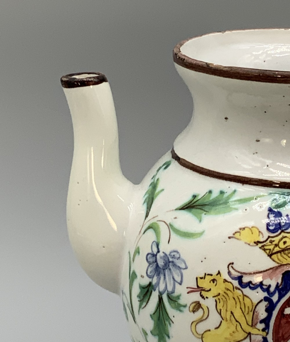 An 18th-century Italian tin-glazed earthenware pharmacy wet drug jug with a spouted body, top handle, lid with sculpted finial, painted armorial crest, floral scrolls, and Latin text reading Syr Alth. View XIII