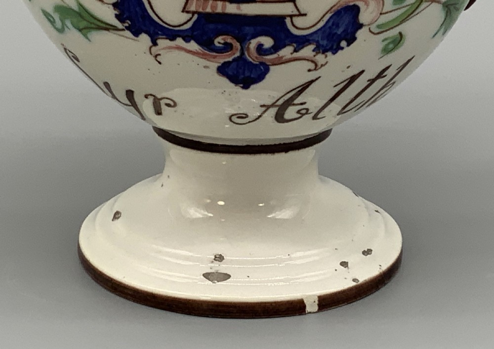 An 18th-century Italian tin-glazed earthenware pharmacy wet drug jug with a spouted body, top handle, lid with sculpted finial, painted armorial crest, floral scrolls, and Latin text reading Syr Alth. View XVI