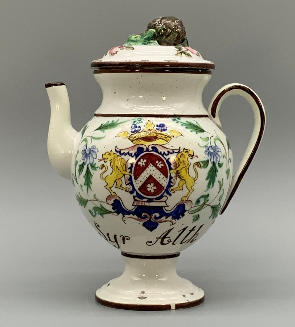 An 18th-century Italian tin-glazed earthenware pharmacy wet drug jug with a spouted body, top handle, lid with sculpted finial, painted armorial crest, floral scrolls, and Latin text reading Syr Alth. View XXI