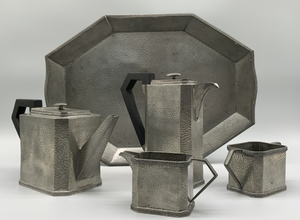 A five-piece Art Deco pewter tea and coffee set featuring a planished finish, geometric handles, and an octagonal tray.