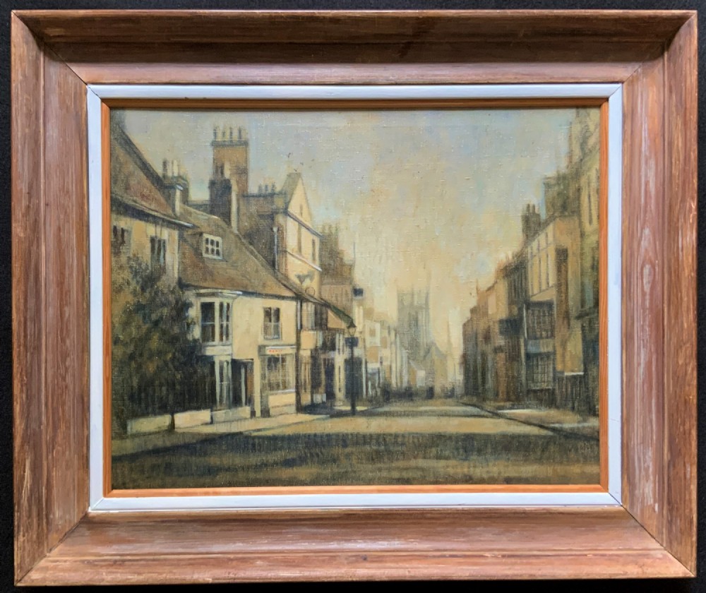 A framed impressionist oil painting depicting a historic street scene with townhouses leading towards a church tower in muted brown, beige, and grey tones.