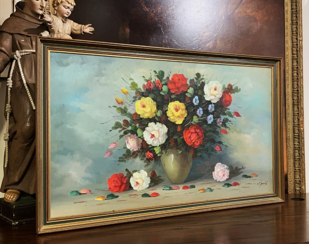 A horizontal framed oil painting on canvas depicting a colourful bouquet of roses and garden flowers in a vase against a blue-grey background.
