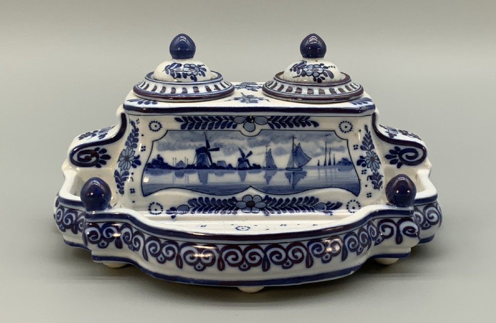A late nineteenth-century Dutch Delft blue and white ceramic inkstand featuring twin removable lids, an integrated pen tray, and hand-painted windmill landscape scenes.