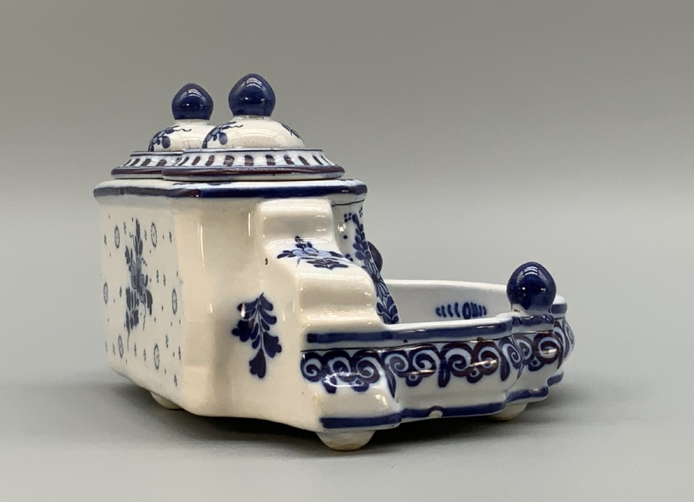 A late nineteenth-century Dutch Delft blue and white ceramic inkstand featuring twin removable lids, an integrated pen tray, and hand-painted windmill landscape scenes. View X