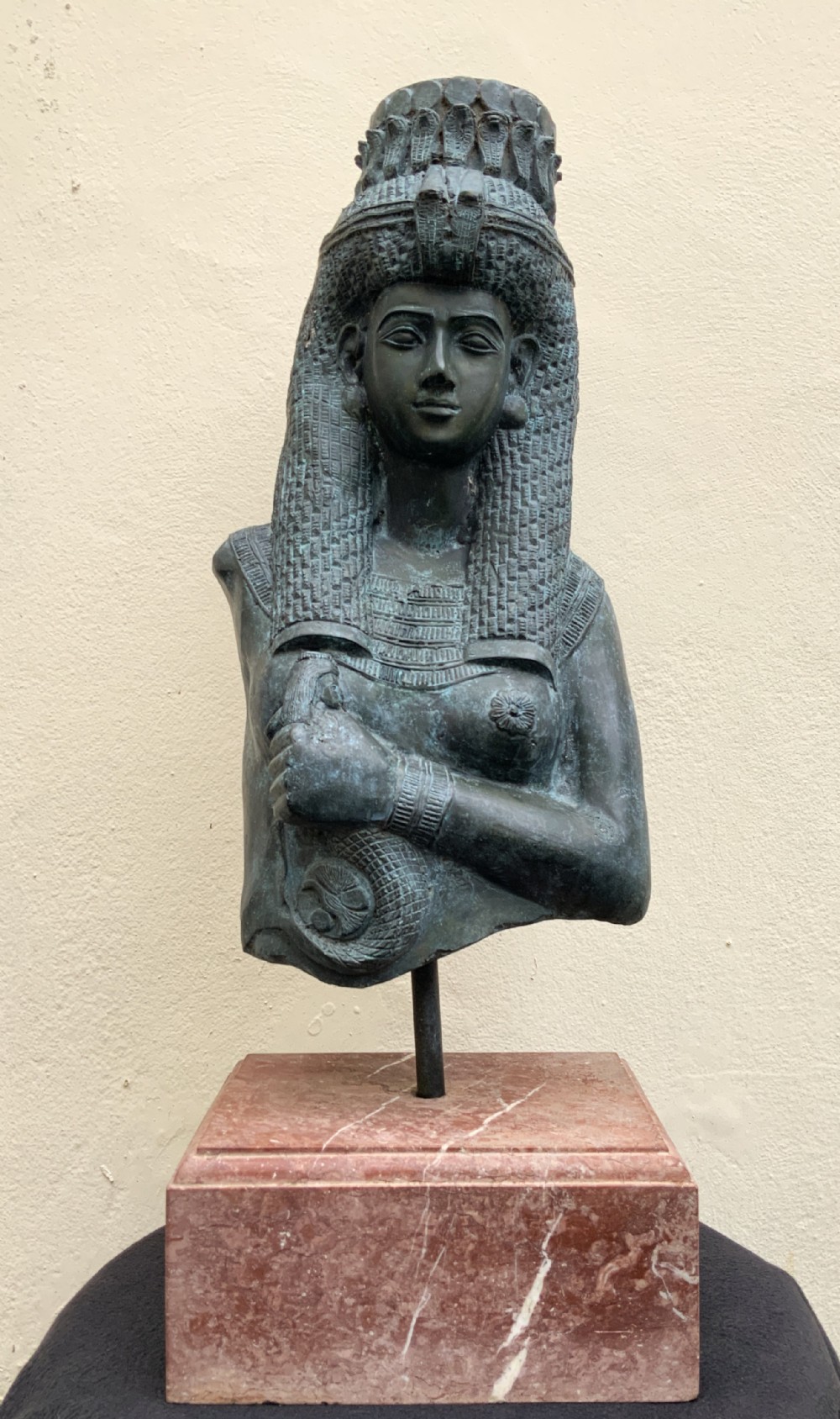 A dark green patinated bronze bust of Cleopatra holding an asp, mounted on a rectangular pink marble base.