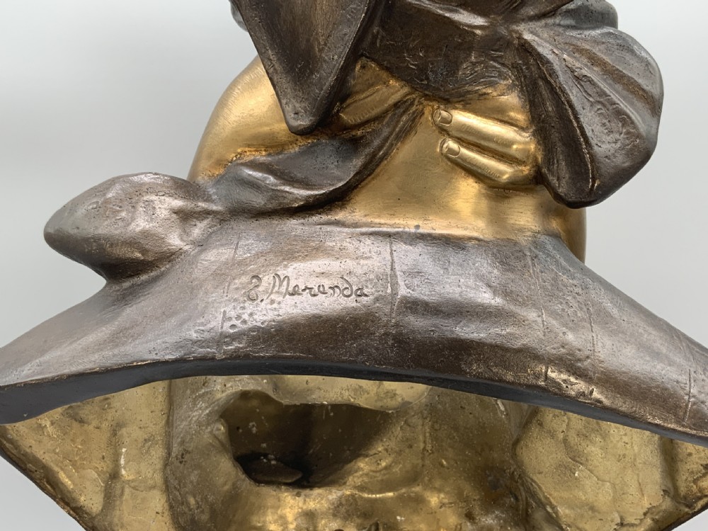 A two-tone bronze bust of a mother wearing a headscarf cradling her infant, mounted on a tall rectangular black veined marble pedestal. View IX