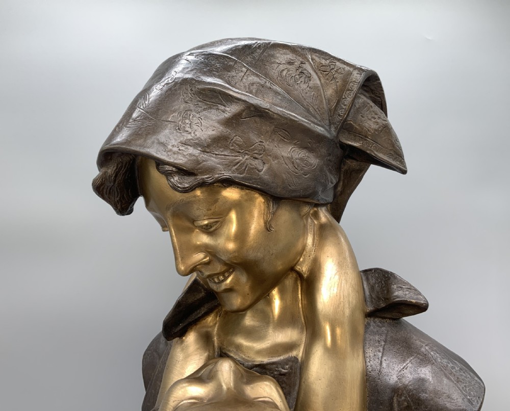 A two-tone bronze bust of a mother wearing a headscarf cradling her infant, mounted on a tall rectangular black veined marble pedestal. View XIV