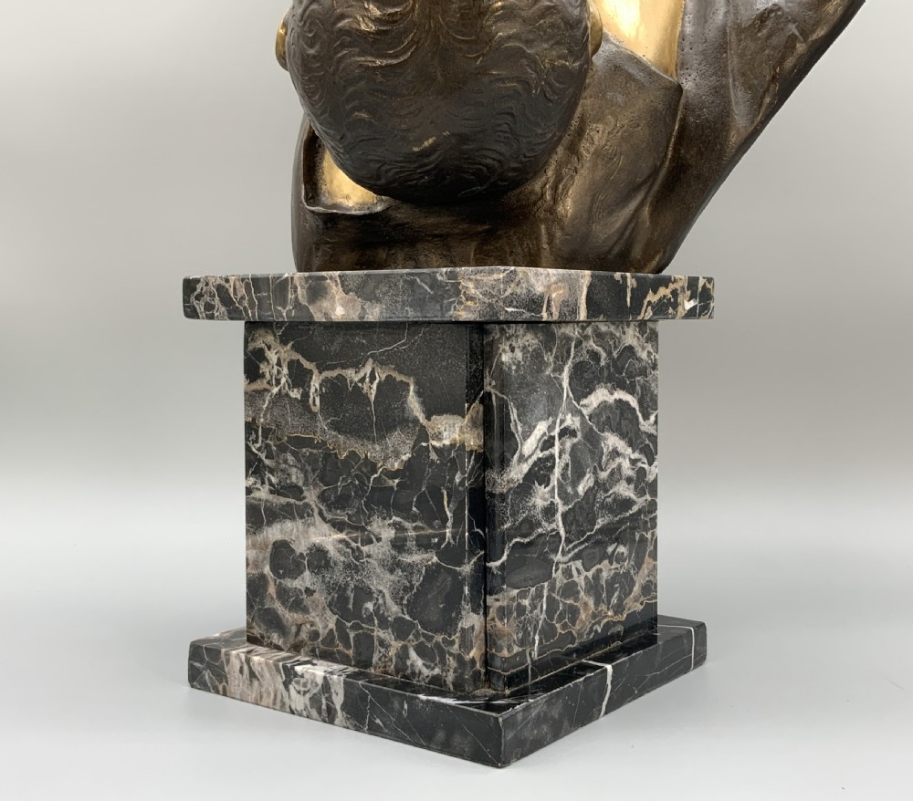 A two-tone bronze bust of a mother wearing a headscarf cradling her infant, mounted on a tall rectangular black veined marble pedestal. View XVI