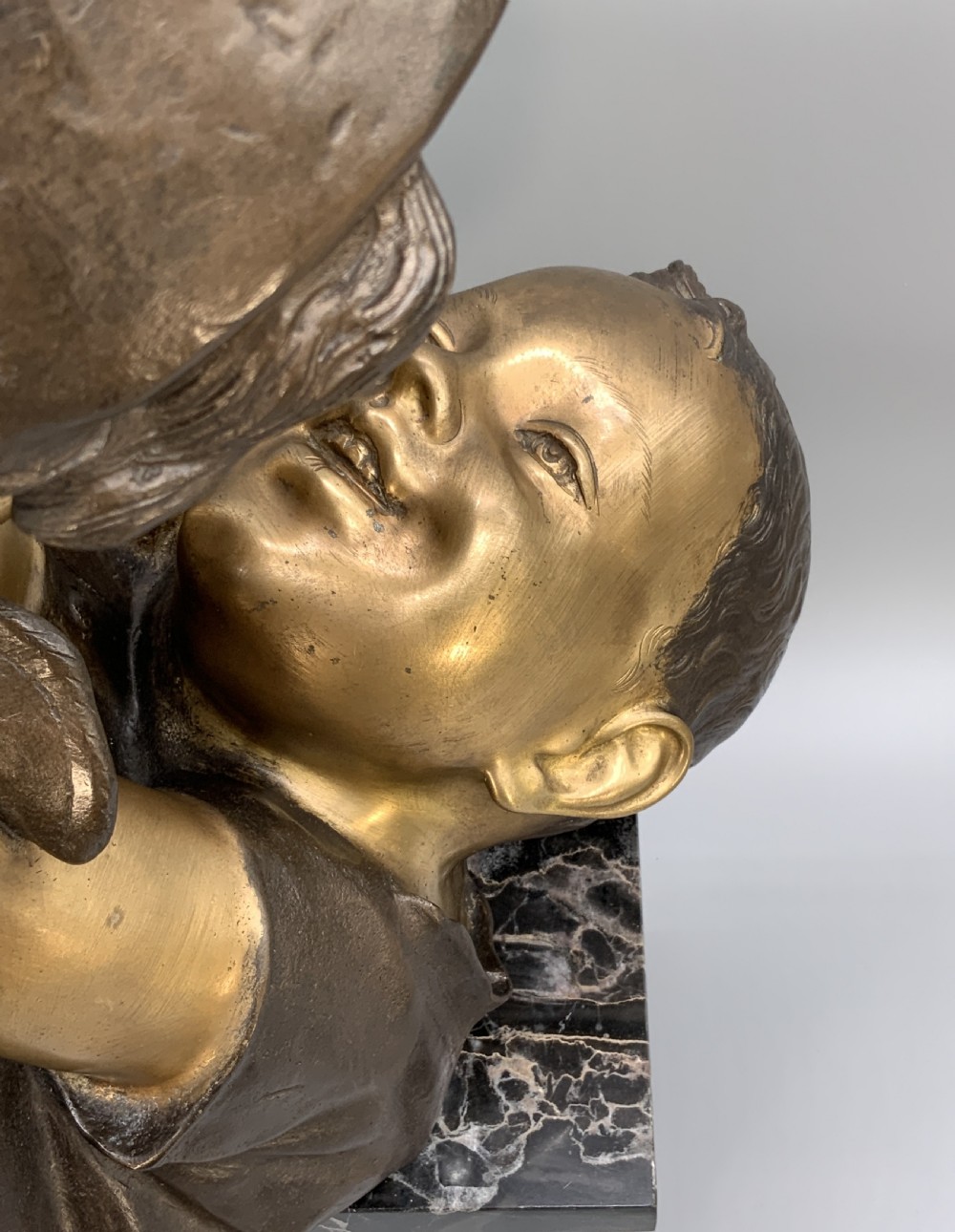A two-tone bronze bust of a mother wearing a headscarf cradling her infant, mounted on a tall rectangular black veined marble pedestal. View XVII