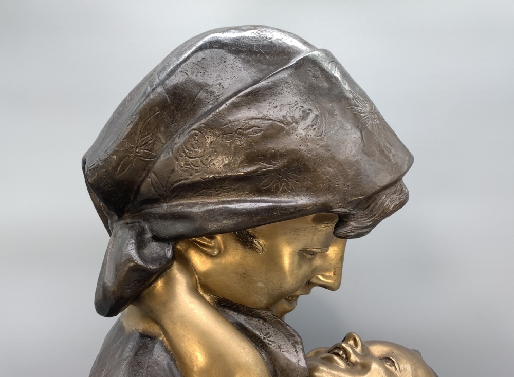 A two-tone bronze bust of a mother wearing a headscarf cradling her infant, mounted on a tall rectangular black veined marble pedestal. View XVIII