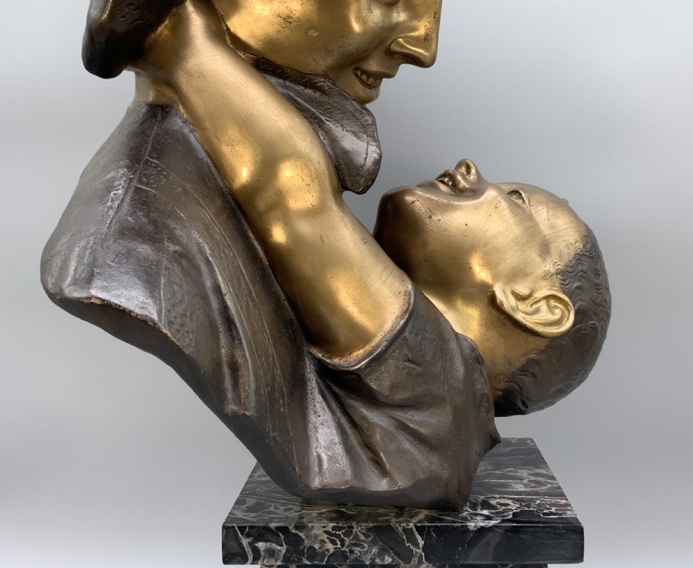 A two-tone bronze bust of a mother wearing a headscarf cradling her infant, mounted on a tall rectangular black veined marble pedestal. View XIX
