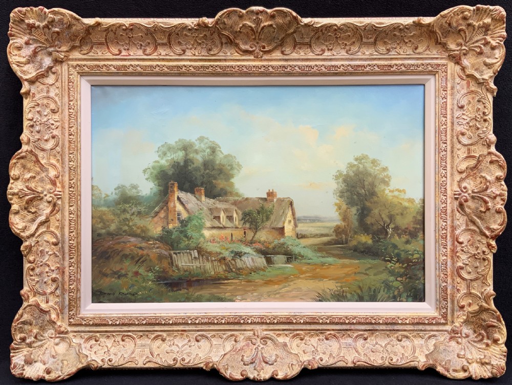 An oil painting depicting a thatched cottage along a dirt lane, housed inside an ornate swept gilt frame with scroll motifs.