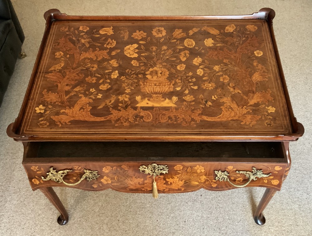 An 18th-century Dutch walnut tea table featuring floral fruitwood marquetry inlays, a tray top, brass handles, and cabriole legs. View XVIII