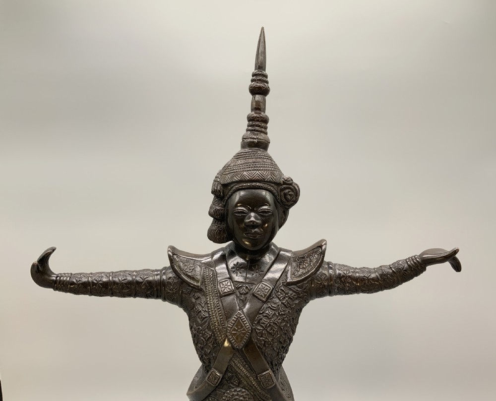 A dark bronze sculpture depicting a classical court dancer in ceremonial attire with a tall spired headdress, balanced on one foot atop an octagonal stepped base. View IX