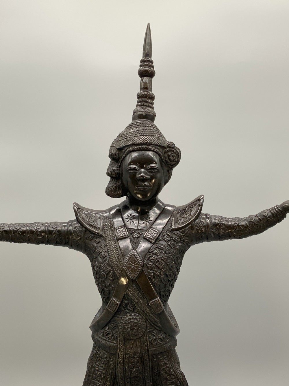 A dark bronze sculpture depicting a classical court dancer in ceremonial attire with a tall spired headdress, balanced on one foot atop an octagonal stepped base. View XIII