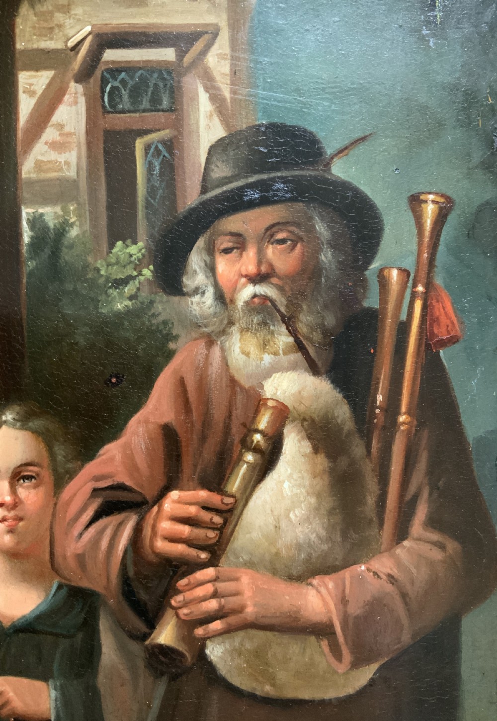 An antique oil painting in a deep burr wood frame depicting an older bearded musician playing a bagpipe alongside a child holding an extended hat. View VI