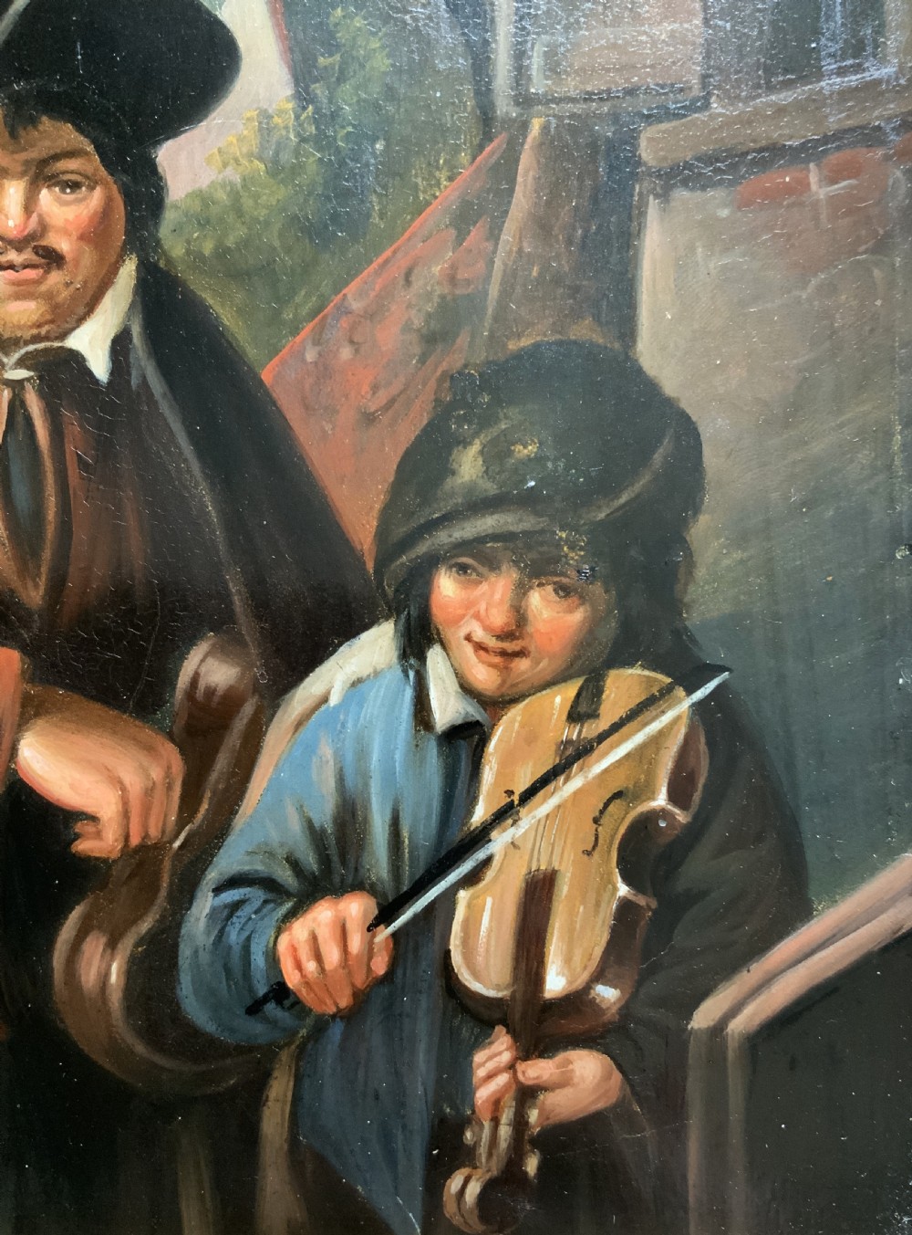 An antique oil painting depicting two musicians, a man and a boy playing a violin, set in a wide wooden frame with a gilded inner moulding. View III