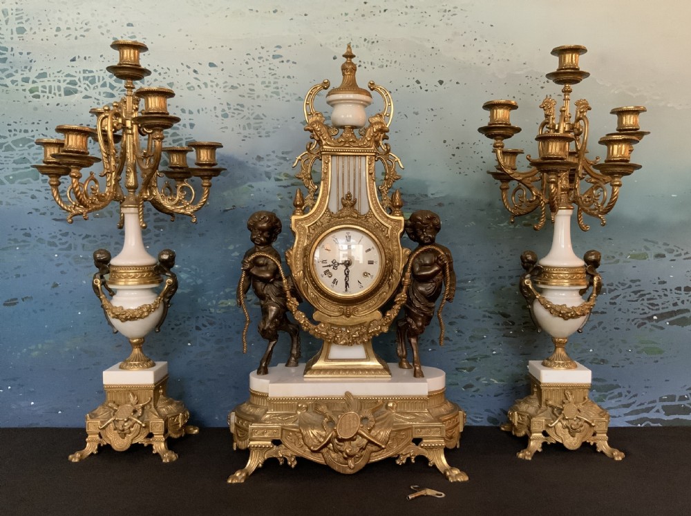 A three-piece antique clock garniture set featuring a central gilt bronze and white marble clock flanked by two matching multi-arm candelabra.