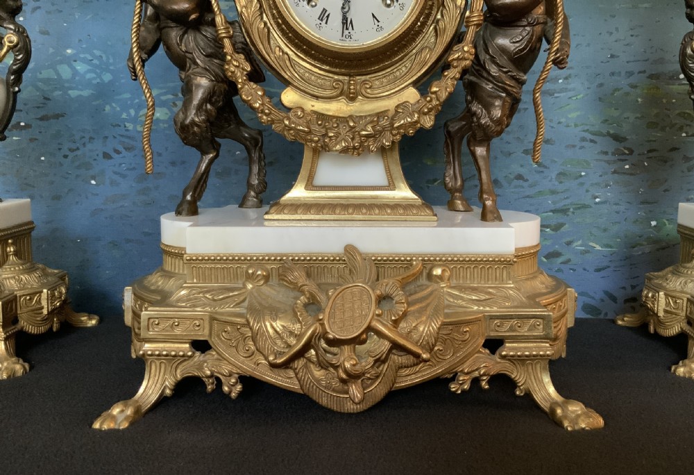 A three-piece antique clock garniture set featuring a central gilt bronze and white marble clock flanked by two matching multi-arm candelabra. View IV