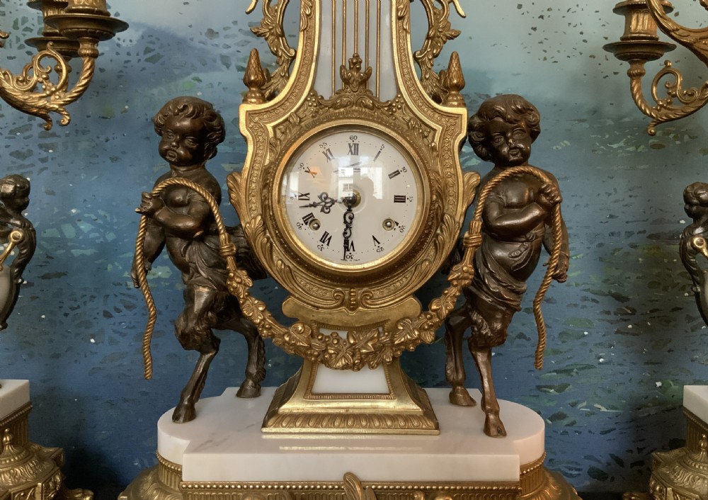 A three-piece antique clock garniture set featuring a central gilt bronze and white marble clock flanked by two matching multi-arm candelabra. View V