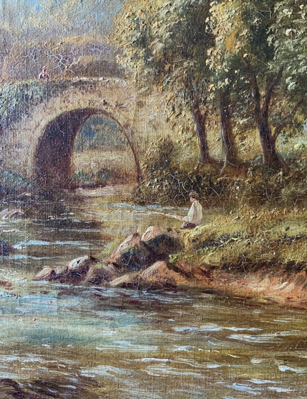 An antique oil painting depicting a tranquil river flowing through a wooded landscape with a stone bridge and cottage in the background, framed in polished dark wood. View XII