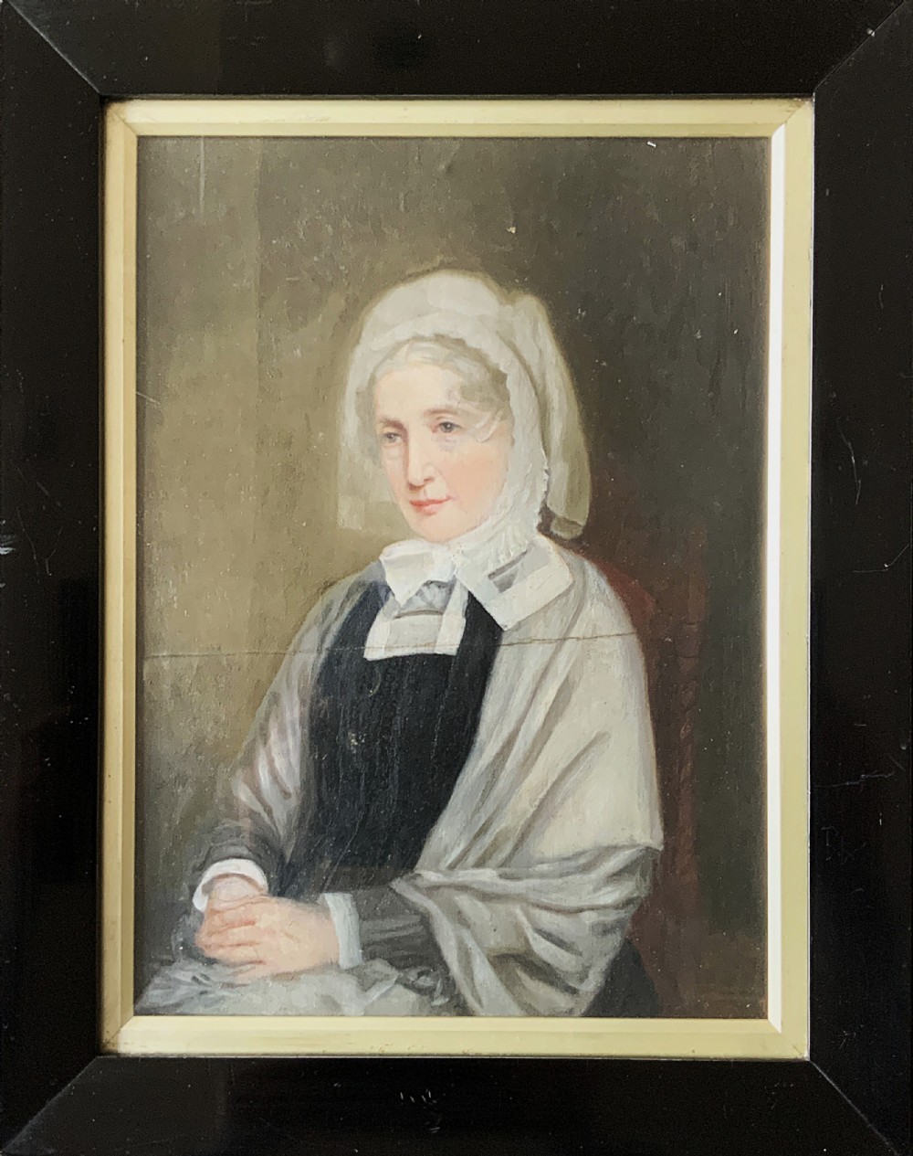 A nineteenth-century oil portrait painting depicting a seated lady wearing a white lace bonnet and grey shawl, housed in a black ebonised frame with a pale inner slip.