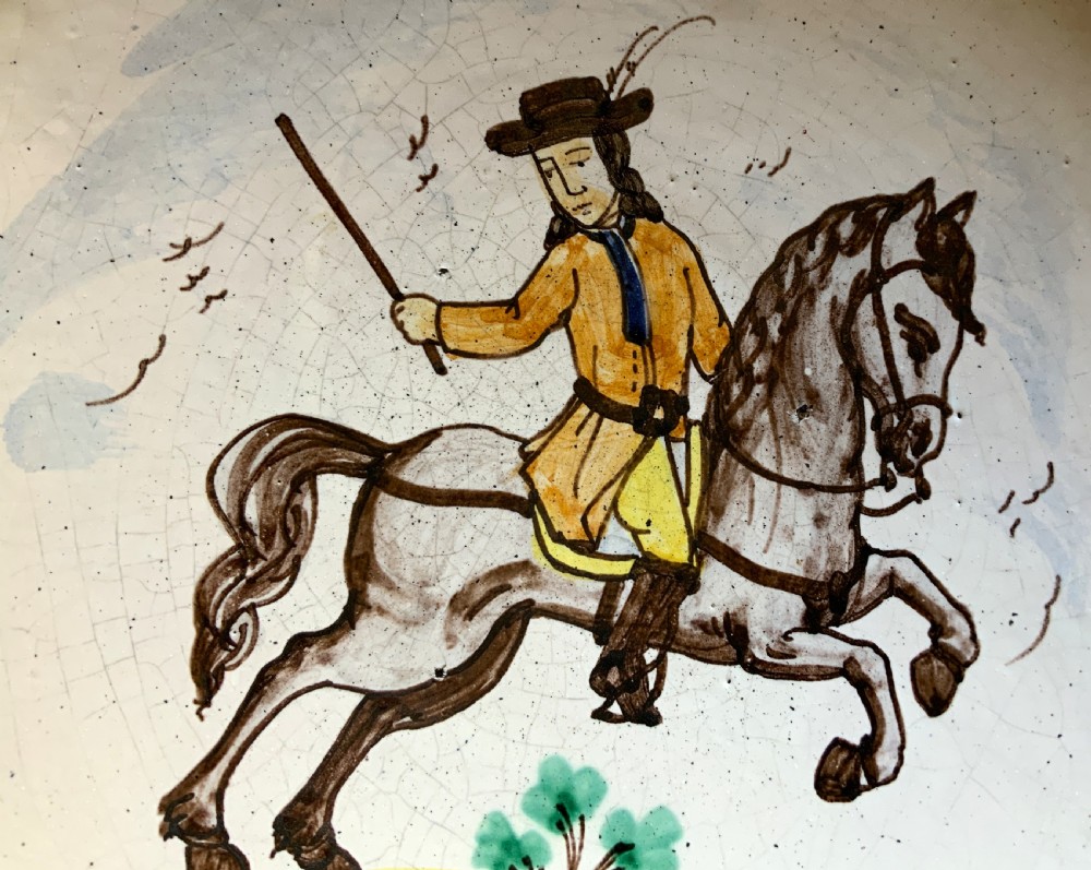 An 18th-century circular Spanish faience charger plate featuring a hand-painted equestrian figure framed by a blue patterned border and a yellow rim. View III