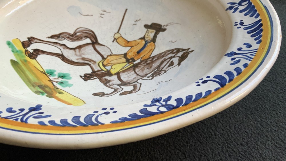 An 18th-century circular Spanish faience charger plate featuring a hand-painted equestrian figure framed by a blue patterned border and a yellow rim. View VIII