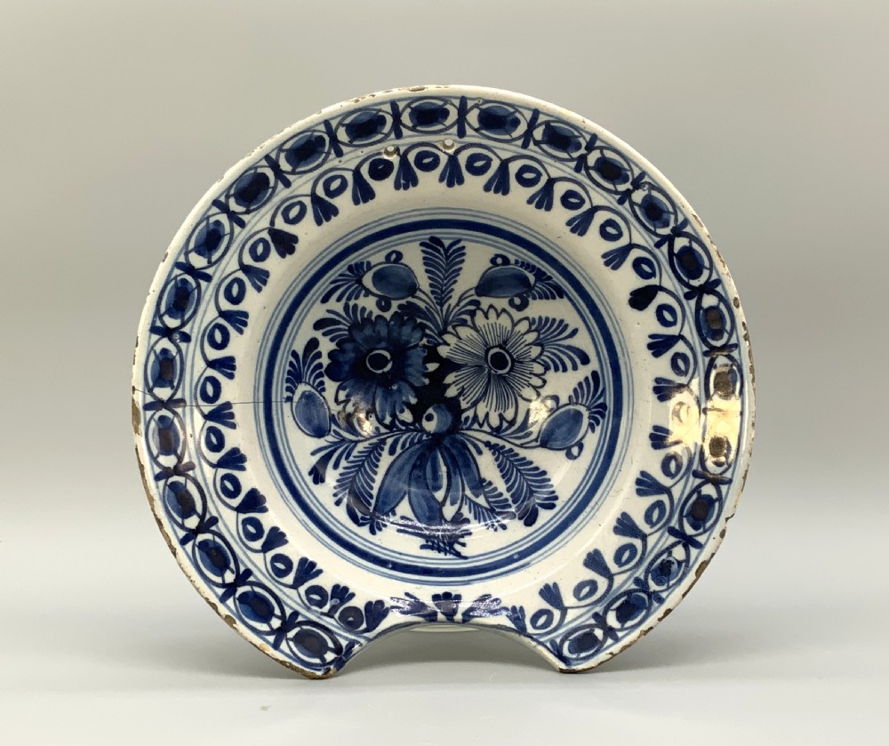 An 18th-century blue and white Dutch Delftware barbers bowl featuring hand-painted floral motifs and a semi-circular rim notch.