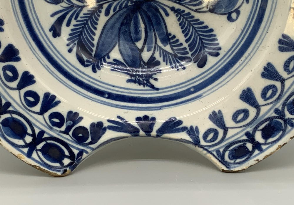 An 18th-century blue and white Dutch Delftware barbers bowl featuring hand-painted floral motifs and a semi-circular rim notch. View VI