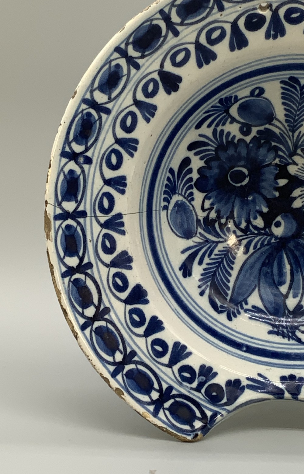 An 18th-century blue and white Dutch Delftware barbers bowl featuring hand-painted floral motifs and a semi-circular rim notch. View VII