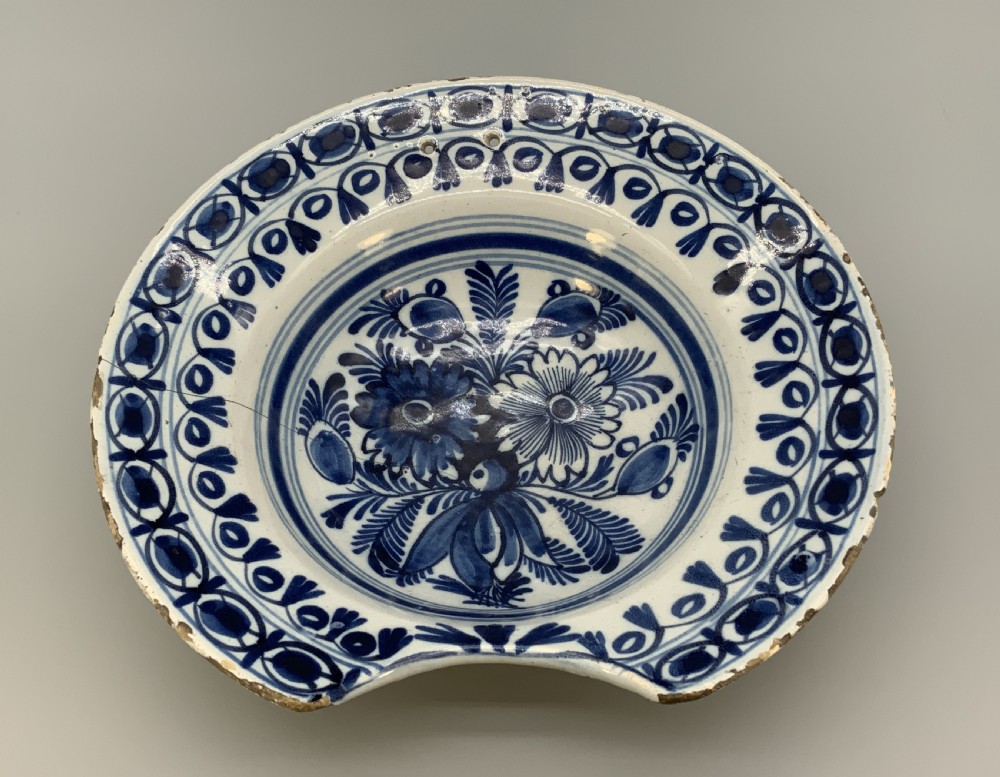An 18th-century blue and white Dutch Delftware barbers bowl featuring hand-painted floral motifs and a semi-circular rim notch. View IX