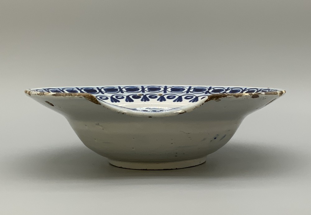 An 18th-century blue and white Dutch Delftware barbers bowl featuring hand-painted floral motifs and a semi-circular rim notch. View XI