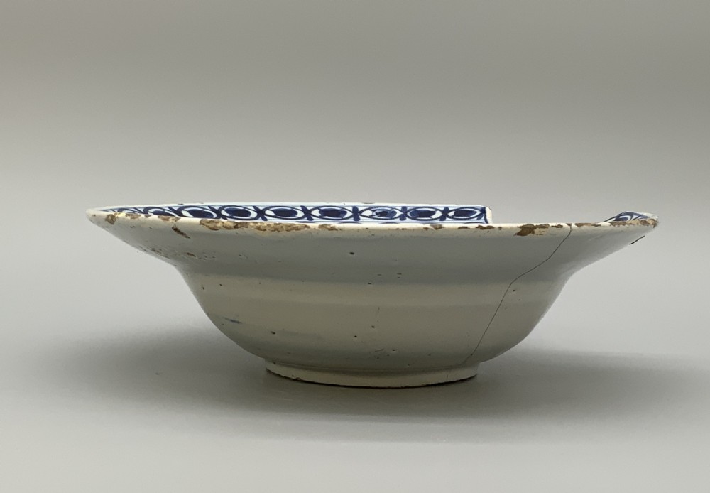 An 18th-century blue and white Dutch Delftware barbers bowl featuring hand-painted floral motifs and a semi-circular rim notch. View XII