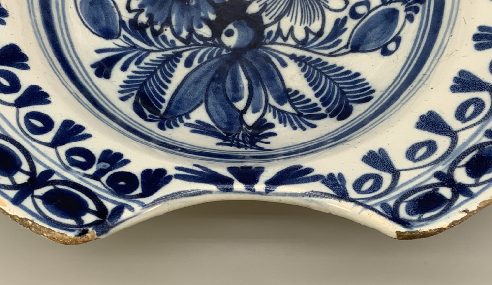 An 18th-century blue and white Dutch Delftware barbers bowl featuring hand-painted floral motifs and a semi-circular rim notch. View XIII