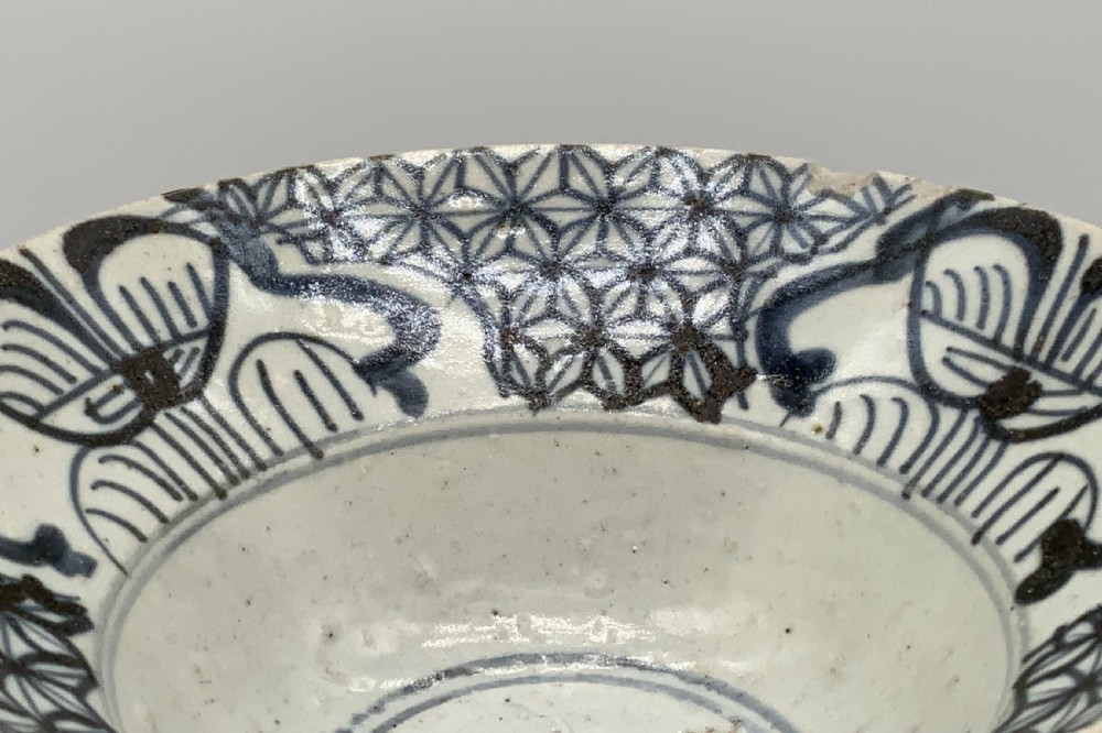 A 17th-century Chinese Swatow porcelain bowl featuring hand-painted underglaze blue geometric and floral motifs on an off-white glazed surface. View IX
