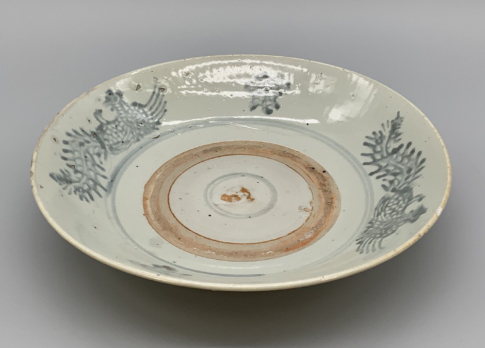 A large circular Ming Dynasty Swatow porcelain charger displaying hand-painted grey-blue phoenix motifs around an unglazed central ring. View X